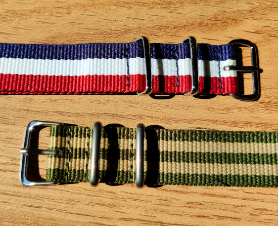 Photographie de deux bracelets NATO cote-à-cote, l'un de couleurs bleu-blanc-rouge et l'autre en deux nuances de vert répétées entre 2 et 3 fois sous la forme de bandes